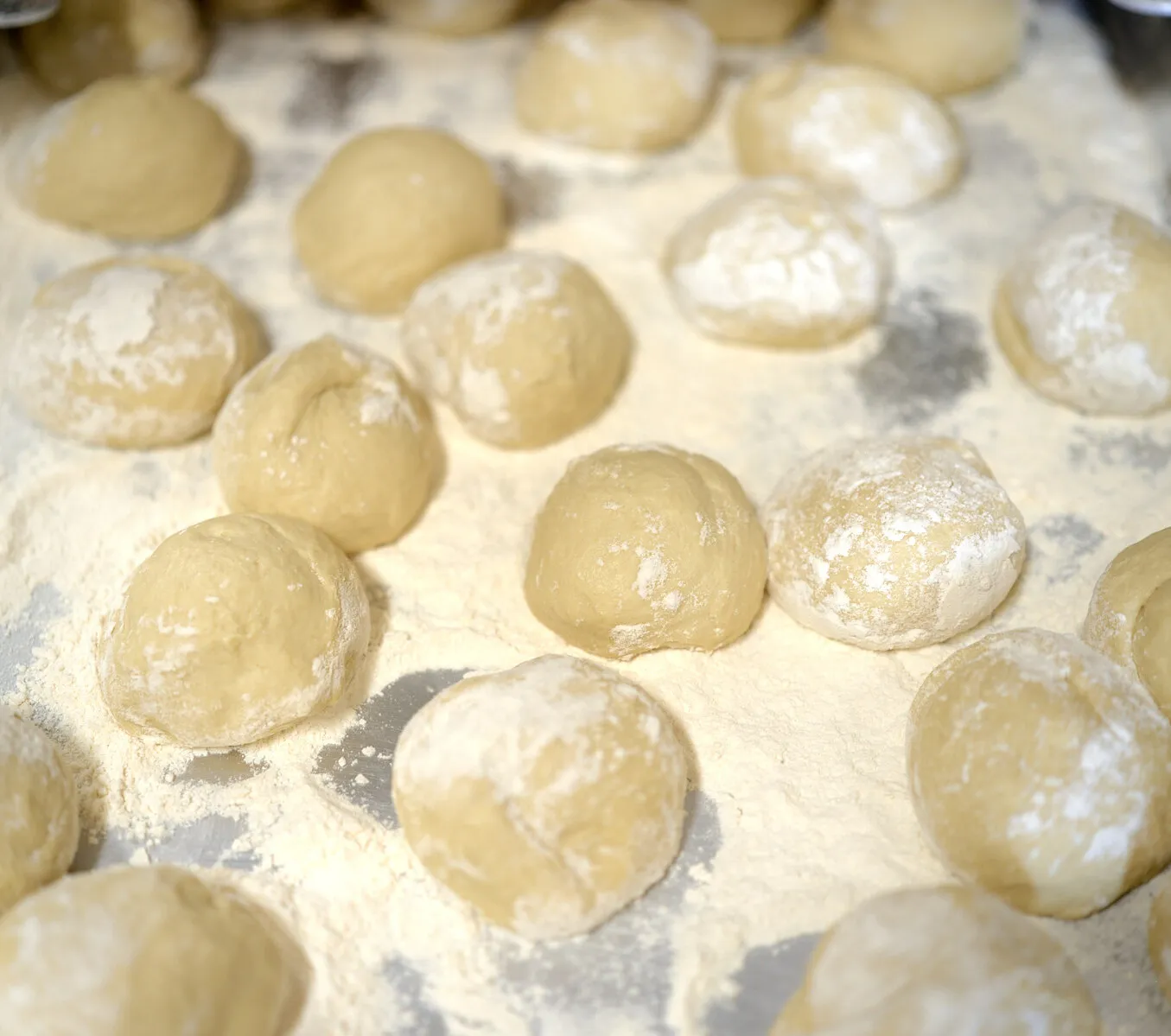 Dough balls resting on a floured tray